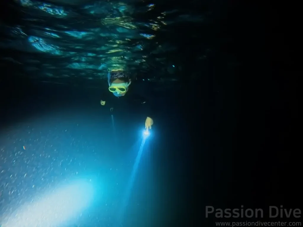 A freediver wearing a mask and holding an underwater flashlight while exploring the mysterious reefs of Cebu.