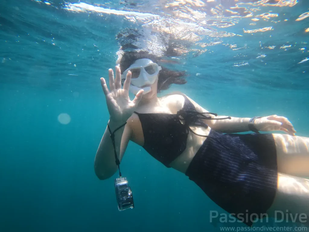 A freediver extending a hand toward the camera underwater at the Passion Dive housereef in Mactan